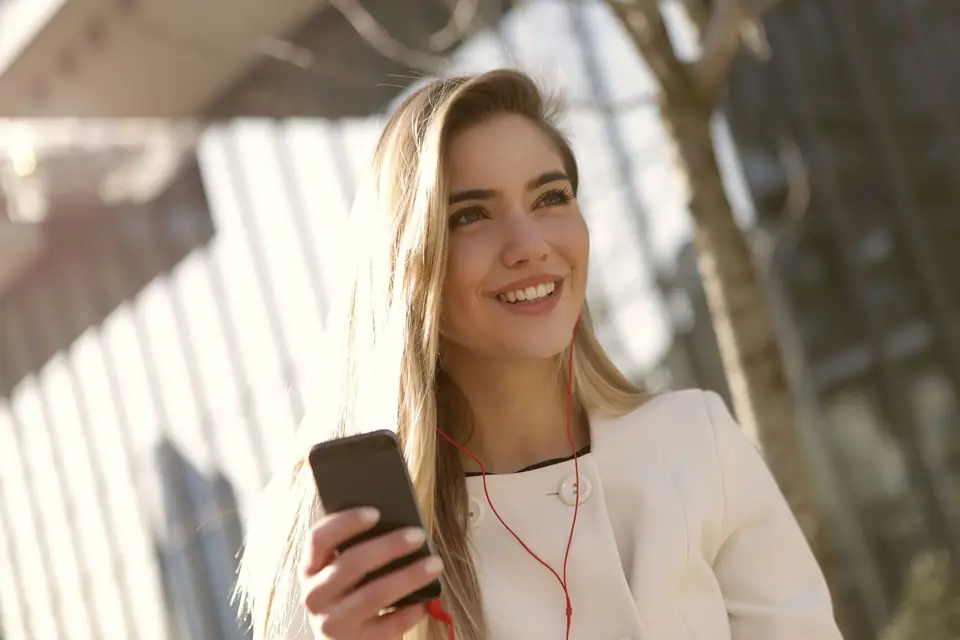 A woman smiling in the sunshine, phone in hand
