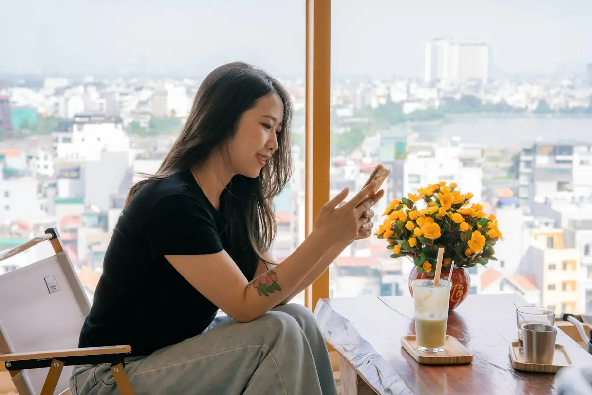A woman smiling at her phone in a sunny cafe with a city view