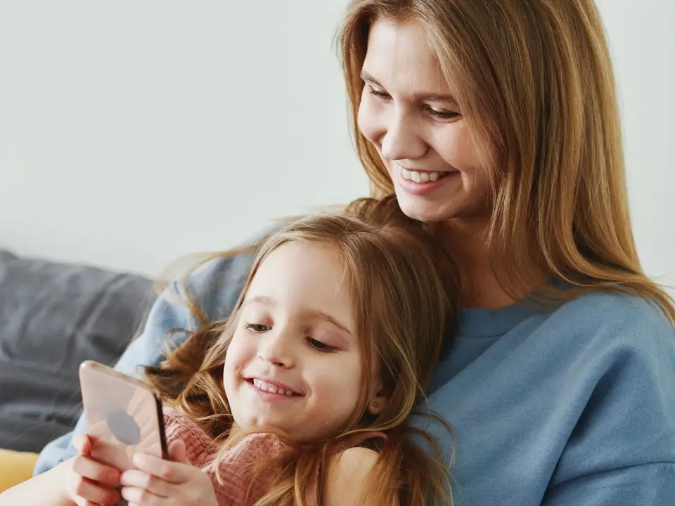 A mother and daughter smiling together over a phone on the sofa
